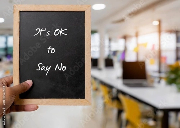 Fototapeta Employee hand holding chalkboard in office with written text  IT'S OK TO SAY NO, means no one can make everyone happy, Stop people pleasing, be true and comfortable to say no when you want to