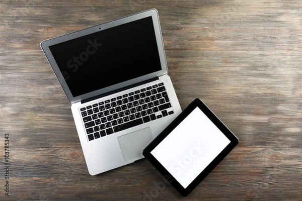 Fototapeta An open silver laptop and modern tablet on the wooden background