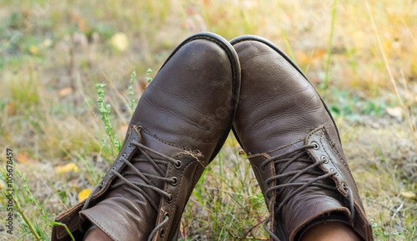 Fototapeta A pair of worn brown leather shoes over the countryside background