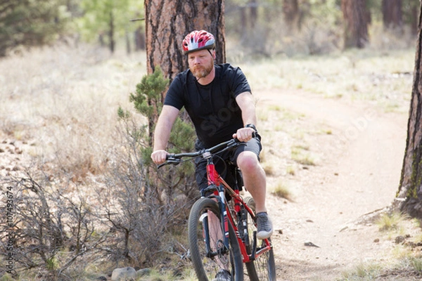 Fototapeta Man riding bike on dirt trail in woods