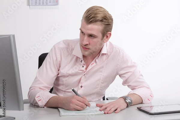 Fototapeta Junger Mann am Schreibtisch mit Formularen und Pad