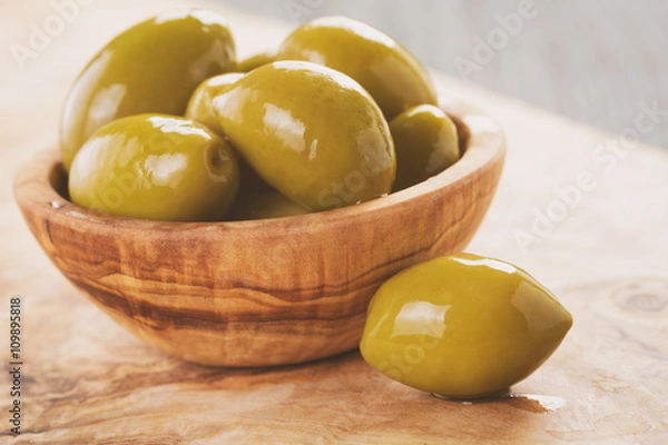 Fototapeta salted giant green olives in olive bowl on wooden table, vintage toned