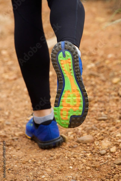 Fototapeta Close up of woman's sneakers running on dirt road