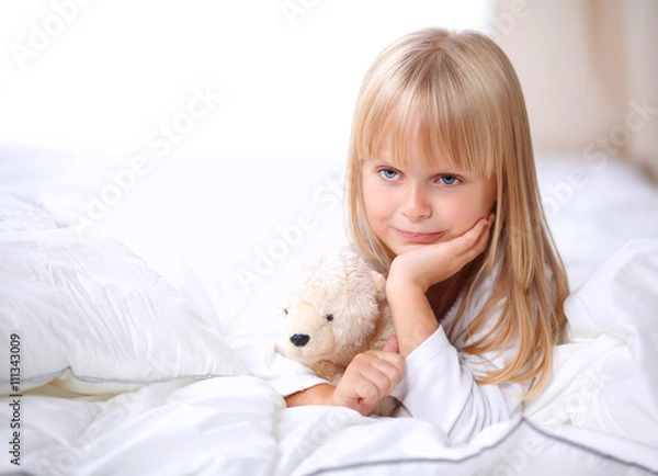 Fototapeta Little girl with teddy bear lying on the bed at home