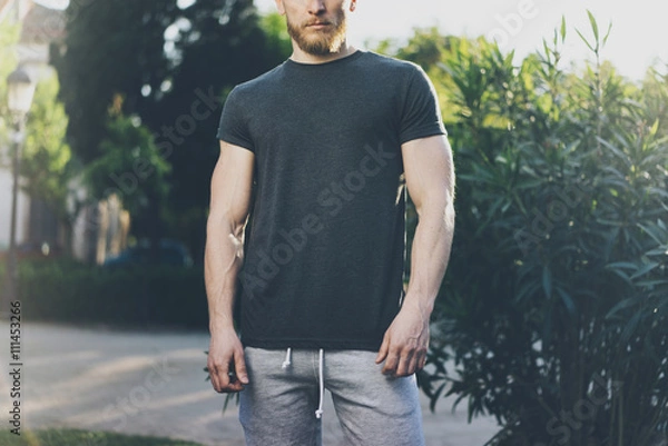 Fototapeta Picture Bearded Muscular Man Wearing Black Empty t-shirt and shorts in summer holiday. Green City Garden Park Background. Front view. Horizontal Mockup.