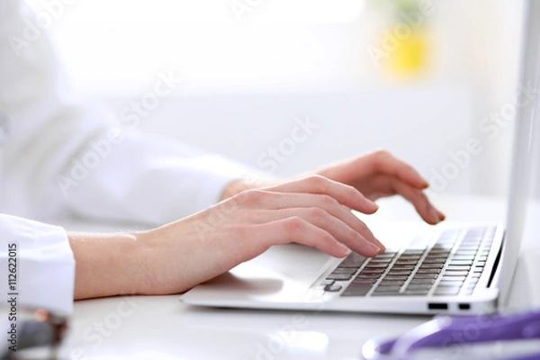 Fototapeta Close-up of female doctor typing laptop sitting at a table in the hospital