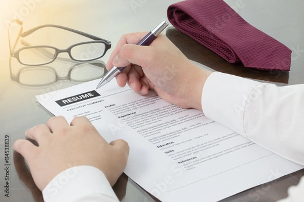 Fototapeta Business man review his resume on his desk or job seeker review his resume before sending to finding a new job. Resume information with pen, notebook, glasses and digital tablet.