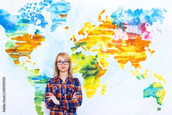 Fototapeta Confident in her knowledge. Cheerful young women holding arms crossed and smiling while standing against map of the world.