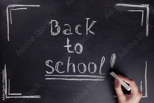 Fototapeta Female hand writes the phrase "Back to school" with white chalk on black chalkboard.