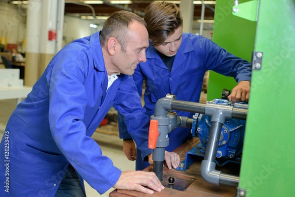 Fototapeta Supervisor watching apprentice use machine