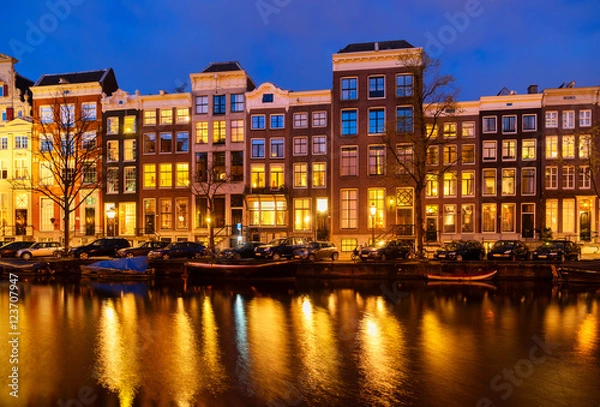 Fototapeta Typical dutch houses over canal with reflections illuminated at night, Amsterdam, Netherlands