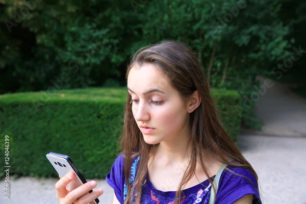 Fototapeta Girl with a mobile phone reads the message in the park