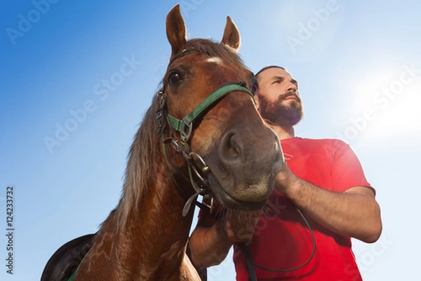 Fototapeta Young man with his bay horse against blue sky