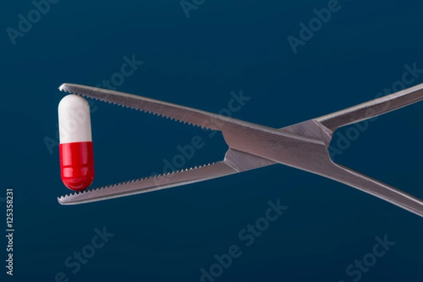 Fototapeta white and red capsule held by medical forceps