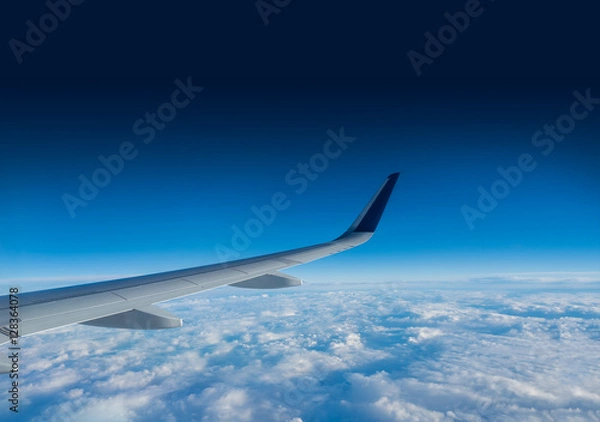 Fototapeta Wing of an airplane flying above the clouds on a clear sunny day