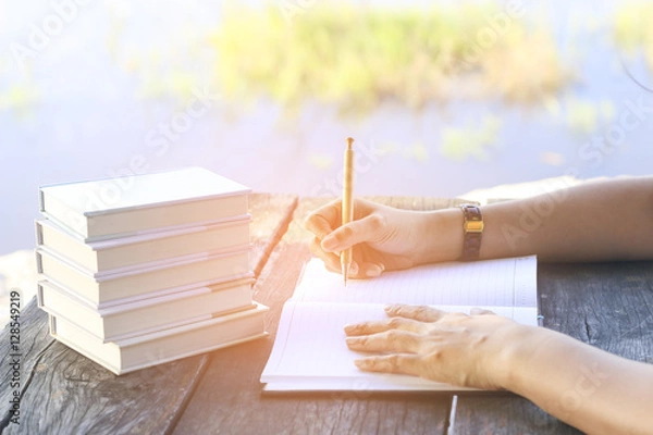 Fototapeta Stock Photo:.female hands with pen writing on notebook on wooden