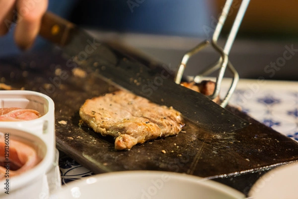 Obraz Hand cutting a slice of pork meat on chopping wood.