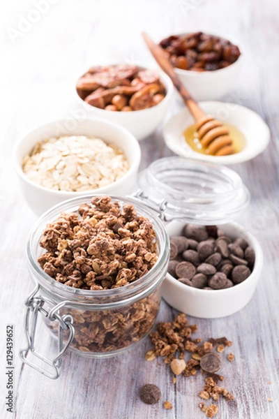 Fototapeta Homemade chocolate granola ingredients, nuts, oats, honey on white wooden background. Healthy breakfast concept.