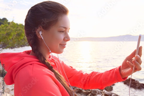 Fototapeta Young woman making selfie at rock beach after run