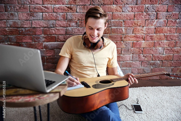 Fototapeta Young man composing a song and sitting on the floor against a brick wall