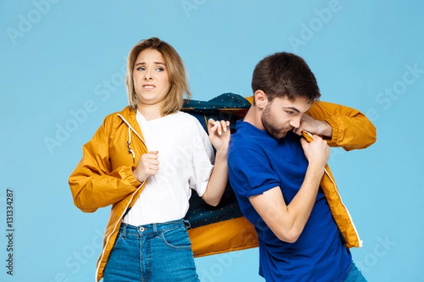 Fototapeta funny young beautiful couple wearing one jacket  over blue background.