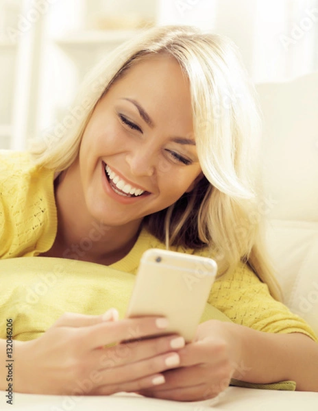 Fototapeta Happy blonde girl with a smartphone at home