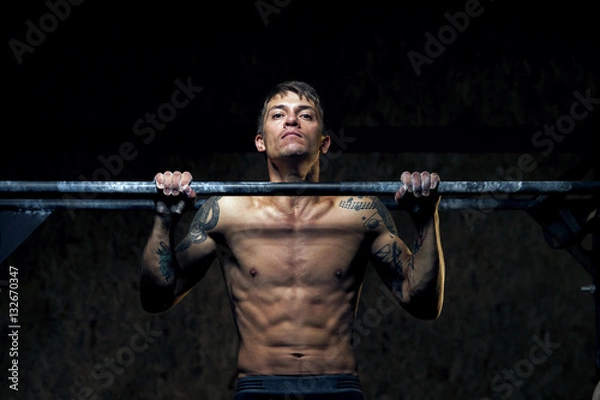 Fototapeta Strong young man doing pull up exercise in gym