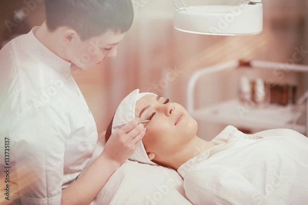 Fototapeta Stylist in white uniform making lengthening lashes