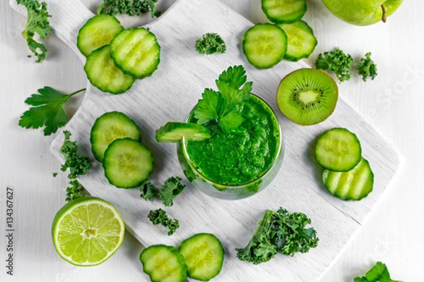 Fototapeta Fresh Green smoothie with kale, cucumber, lime, apple, parsley on white board.