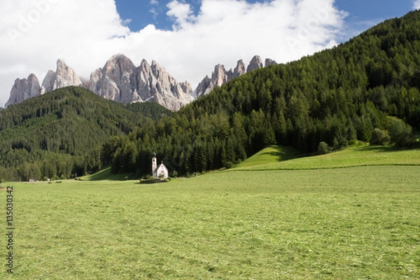 Fototapeta The symbol of the valley Val di Funes - church of Santa Maddalena. Rocky peaks and forested mountains surrounded by green Alpine meadows. Tirol, Dolomites. Sunny warm autumn day