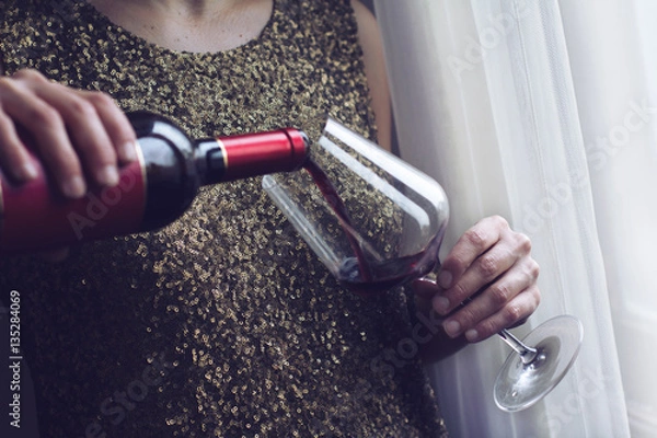 Obraz woman with gold spangle dress pouring red wine into a glass