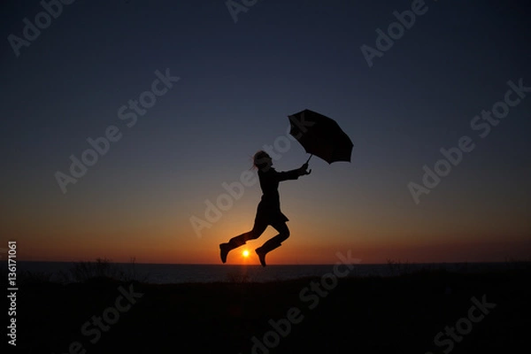 Obraz silhouette of a girl with an umbrella at sunset jumping