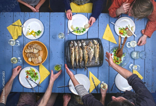 Fototapeta Top view on people eating grilled fish with vegetable salad and drinking vine.