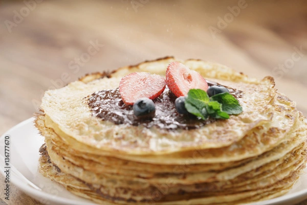 Fototapeta fresh blinis or crepes with melted dark chocolate, berries and sugar powder, shallow focus