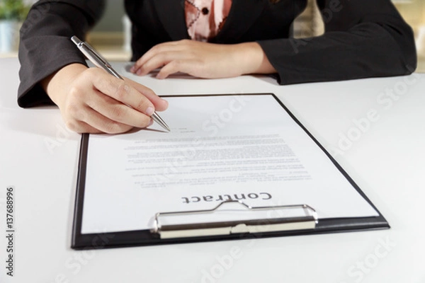 Fototapeta Hands of business woman signing the contract document with pen on desk - business concept