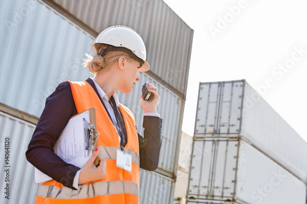 Fototapeta Female engineer using walkie-talkie in shipping yard