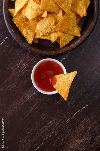 Fototapeta Nachos chips. Delicious salty tortilla with sweet salsa or chilli sauce on wooden background. Snack on rustic plate.