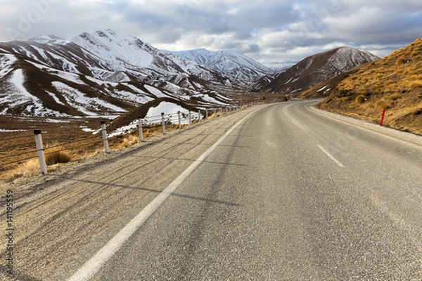 Fototapeta A winding alpine road disappears into the distance amongst snow capped mountains in New Zealand.