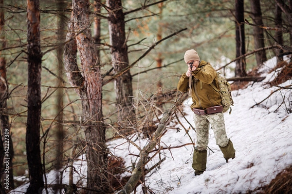 Fototapeta Female hunter in camouflage clothes ready to hunt, holding gun and walking in forest.