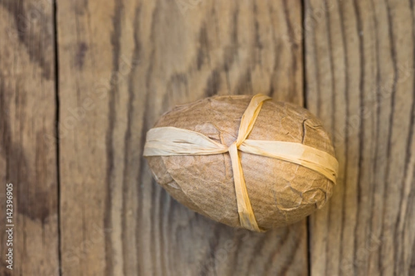 Fototapeta Handcrafted decorative Easter egg wrapped in craft paper tied with twine on plank wood background, conceptual