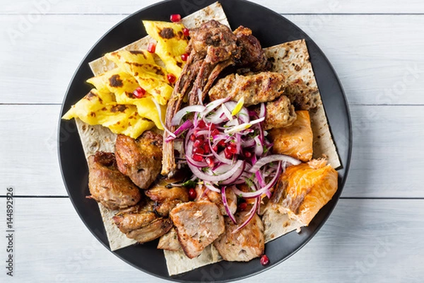 Fototapeta Lyulya kebab, shish kebab, grilled salmon fish, onion and pomegranate grains on black plate and white wooden table. Top view