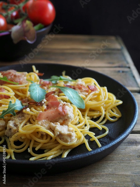 Fototapeta Spaghetti carbonara in black pan and fresh tomatoes on wooden table.