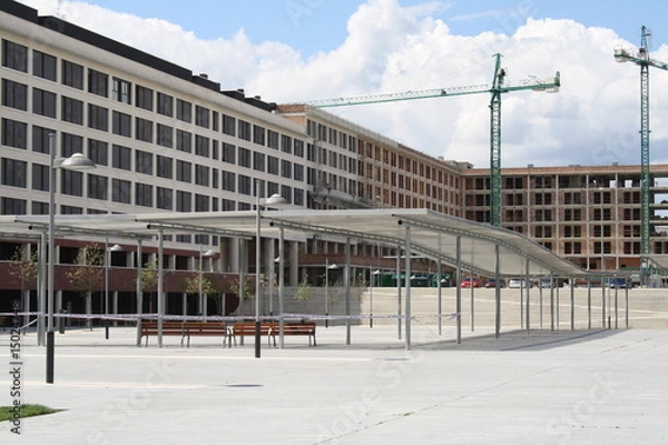 Fototapeta Edificio en construccion junto a plaza con emparrado.