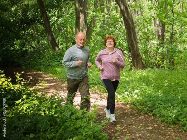 Fototapeta Older couple wearing sportswear and running in forest at mountain