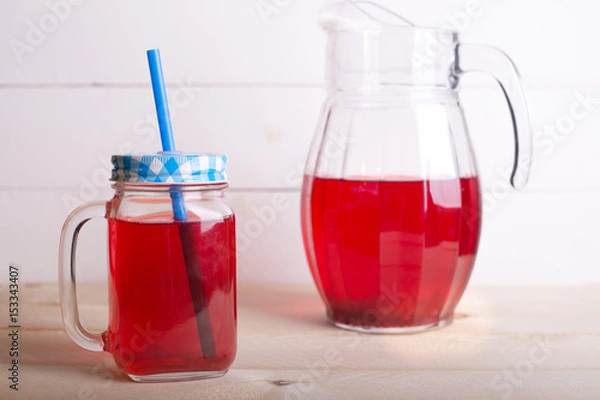 Fototapeta Fresh and healthy red Fruit juice drink  in a glass and jug on the wooden white table background. Side view.