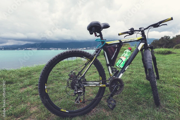 Fototapeta A bicycle stands on a green lawn of the sea coast with a view of the mountain range concept of active recreation and healthy lifestyle