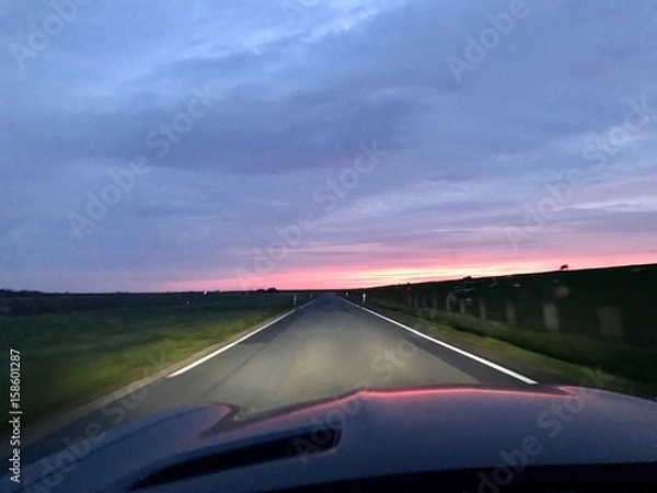 Fototapeta Bei Sonnenuntergang mit dem Auto auf der Landstraße unterwegs