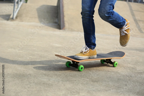 Fototapeta skateboarder legs riding skateboard at skatepark