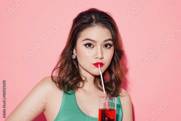 Fototapeta Happy fashion asian woman drinking champagne over pink background.