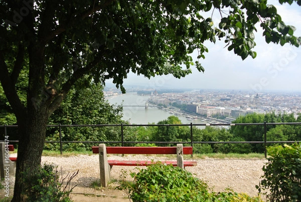 Fototapeta A viewpoint at the park over the hill at Budapest, a view to Danube river and a building of Parliament and a bench under a three, Hungary.